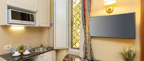 Cocina compacta con microondas, lavamanos y un refrigerador pequeño. Hay una mesa de comedor con una revista y una planta en maceta.