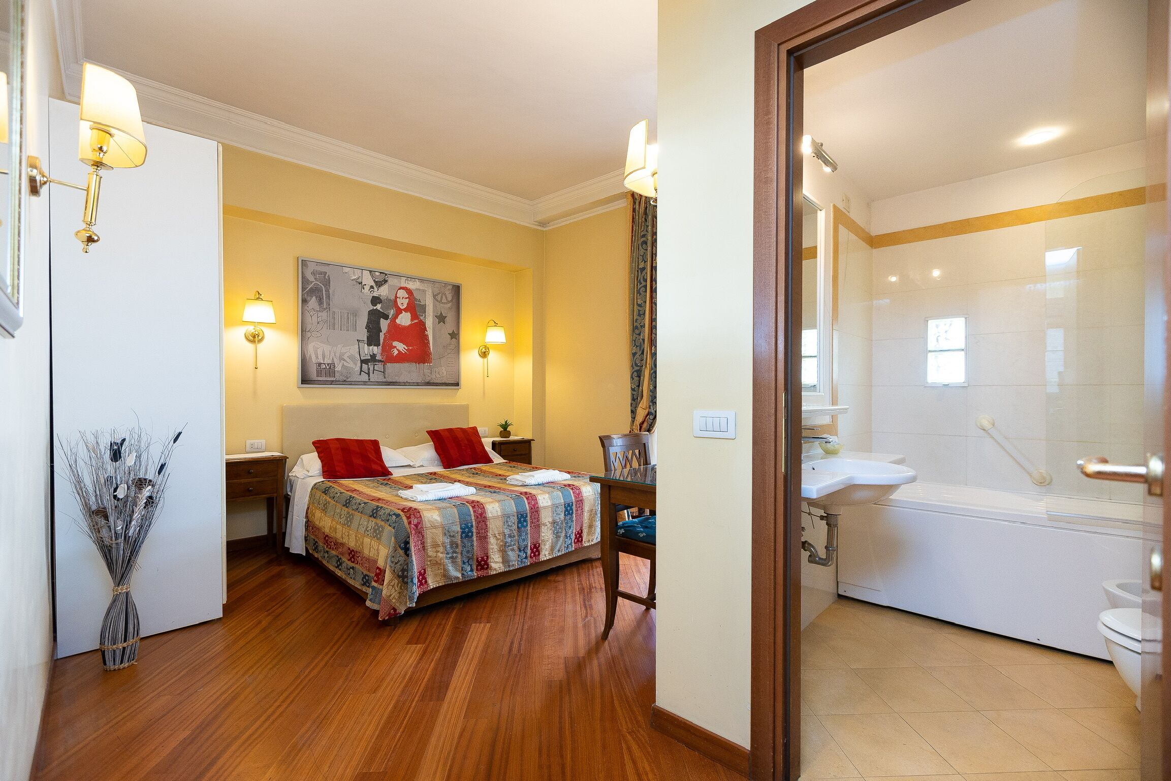 A hotel room with a bed, bedside table, lamp, and a bathroom with a bathtub and toilet.
