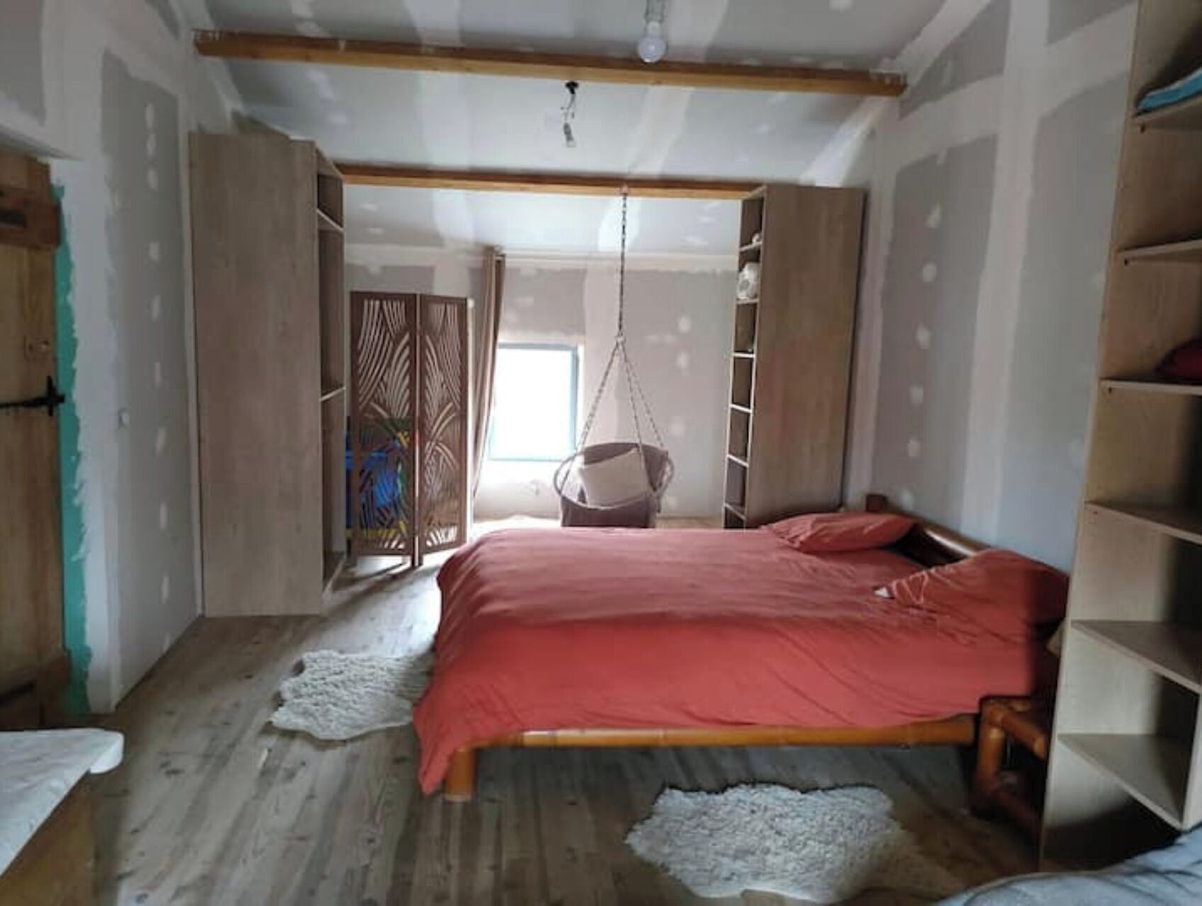 Un dormitorio con cama, una silla colgante y un armario.