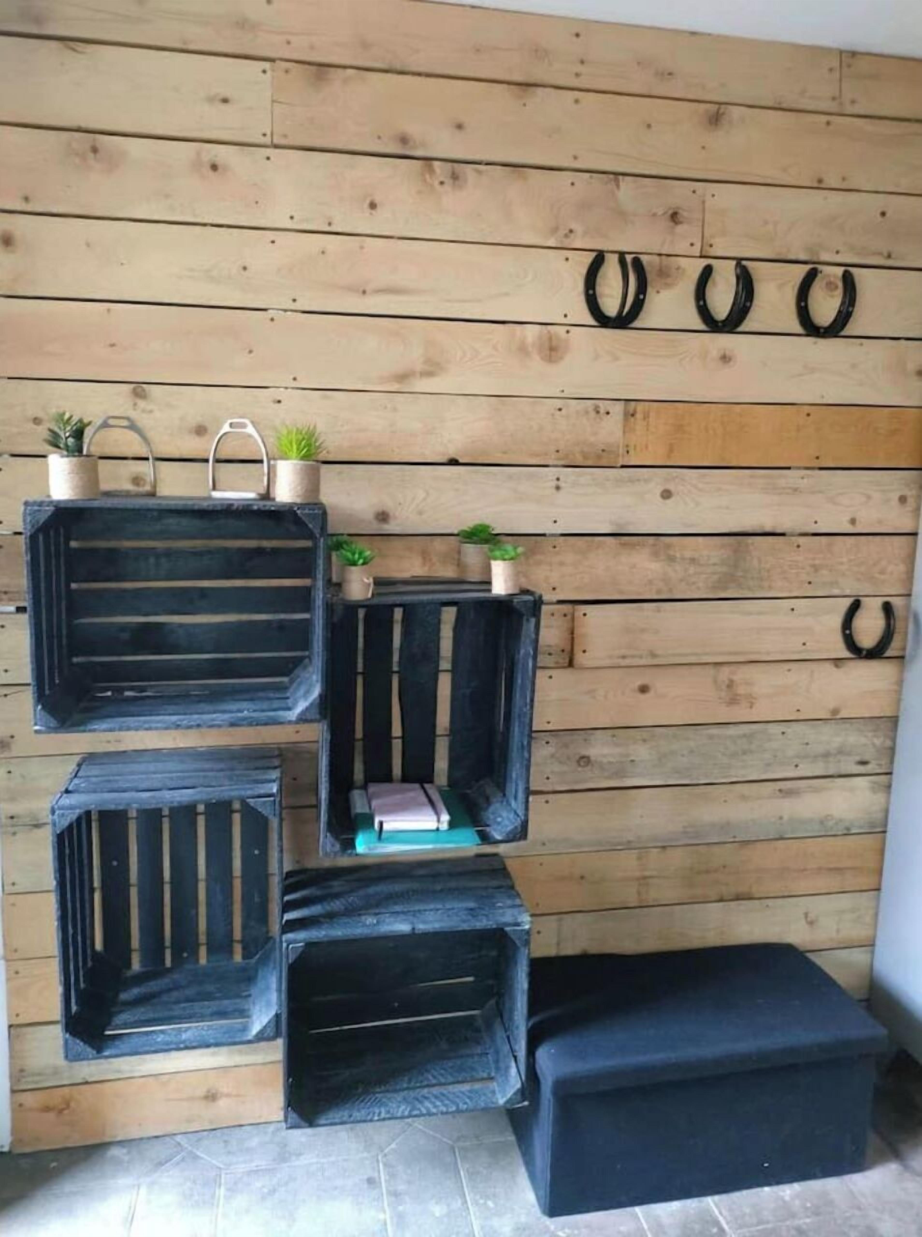 Ein Zimmer mit einer Holzwand und drei schwarzen Aufbewahrungsbehältern mit Tragegriffen, einem kleinen Regal mit Topfpflanzen sowie einem schwarzen Hocker.