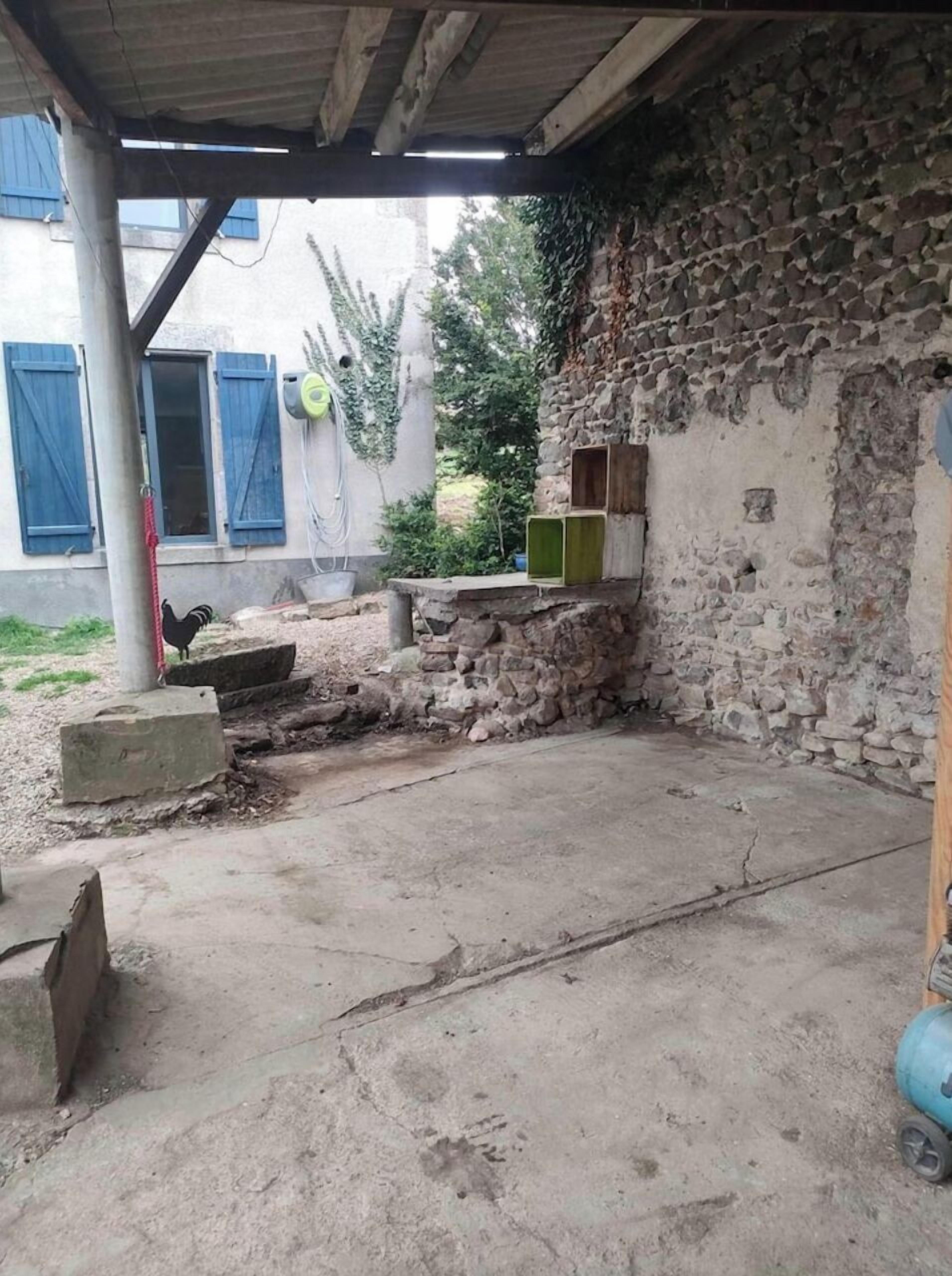 Un espacio al aire libre rústico con pared de piedra, suelo de concreto y una estructura de madera con cajas verdes y marrones.