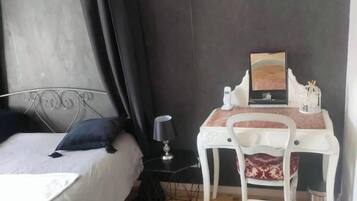 A bedroom with a bed, a bedside table with a lamp, a chair, a small table with a picture, and a curtain.