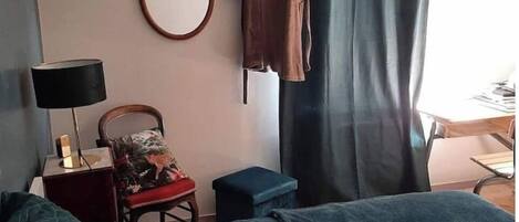 Un dormitorio con cama, una silla, una mesita, un espejo y una bata colgada en la pared.