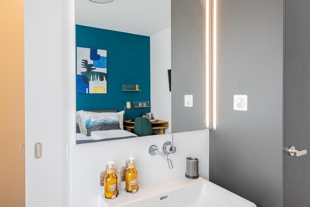 Un baño moderno con un lavamanos blanco, dos botellas de jabón para manos, un espejo y una pared azul con obras de arte.