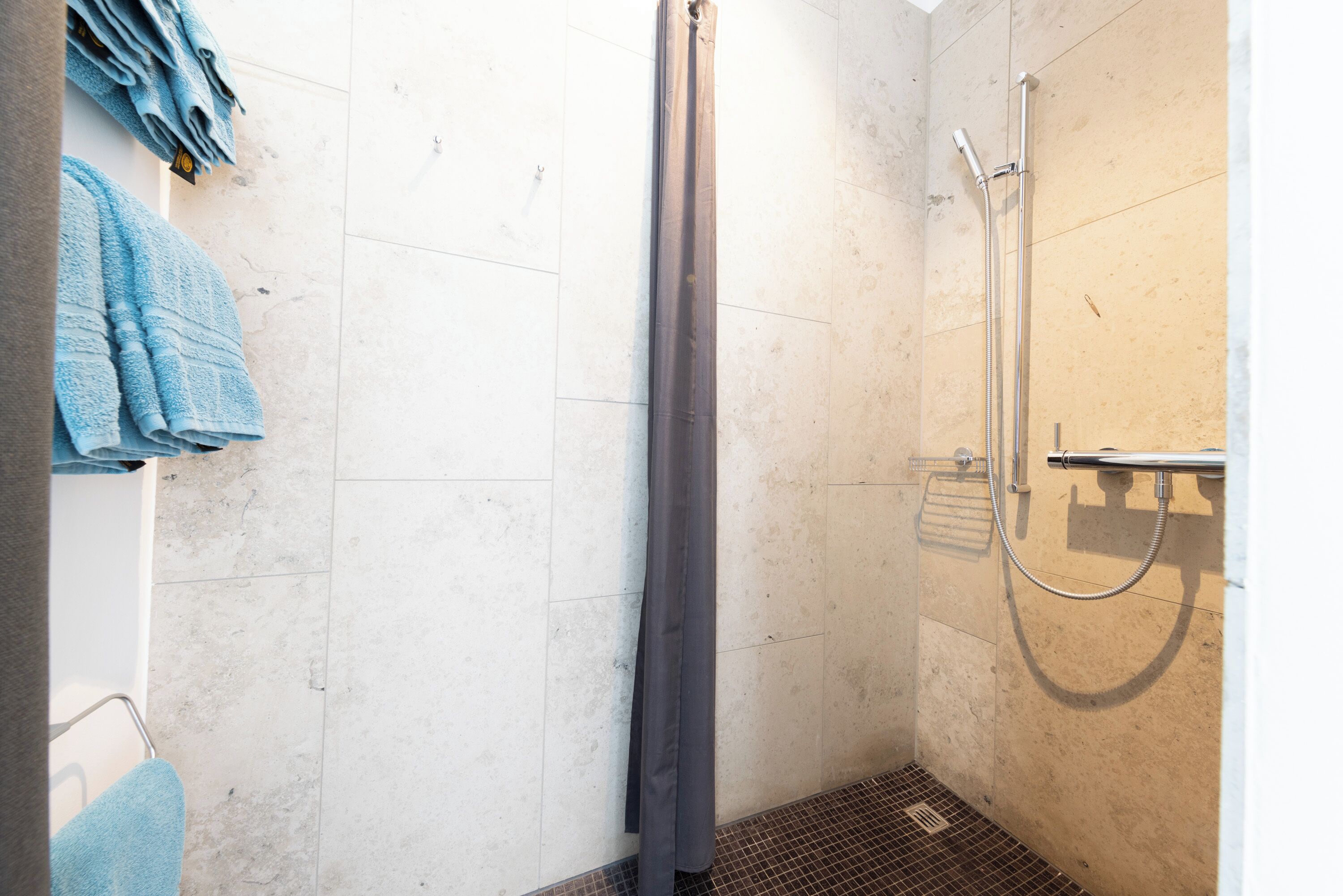 A shower area with a shower curtain, a handheld showerhead, and a towel rack with folded towels.