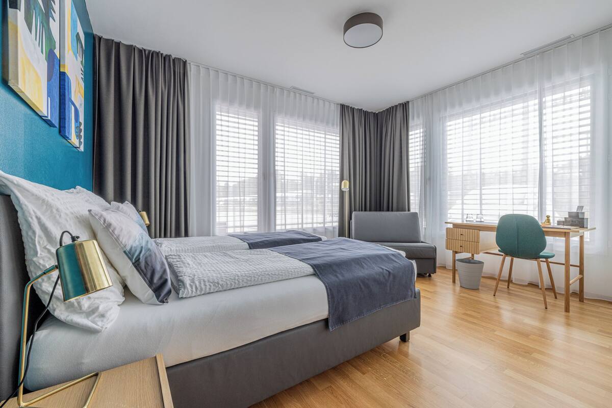 A modern hotel room with a large bed, a desk, and a chair.