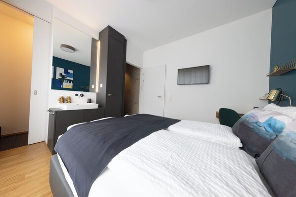 A modern bedroom with a large bed, a built-in wardrobe, a small desk, and a mirror. - Ambrosia Guesthouse (Rheinfelden)