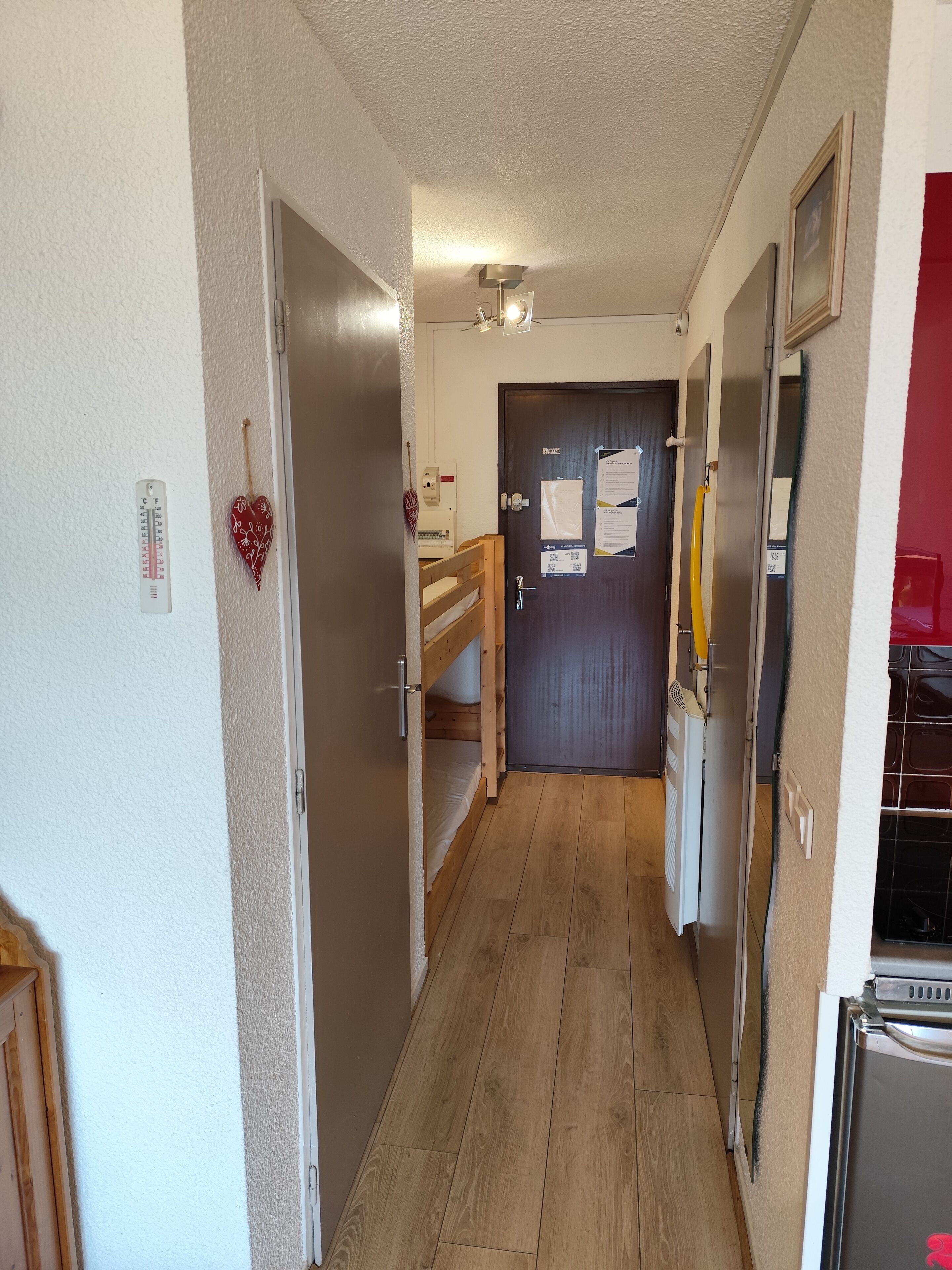 Ein schmaler Flur mit Holzboden, einer Tür am Ende und einem Kühlschrank zur rechten Seite.