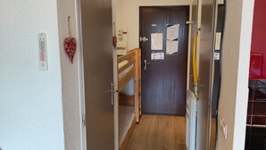 A narrow hallway with wooden flooring, a door at the end, and a refrigerator on the right. - Résidence Plein Sud, Front de Neige Centre, à Côté Télécabine 3400m (Les Deux Alpes)