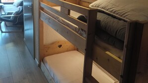 A bunk bed room with a wooden headboard, a small bedside table, and a wall-mounted light. - Résidence Plein Sud, Front de Neige Centre, à Côté Télécabine 3400m (Les Deux Alpes)