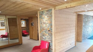 A modern interior with wooden paneling, a stone accent wall, and red seating. - Résidence Plein Sud, Front de Neige Centre, à Côté Télécabine 3400m (Les Deux Alpes)