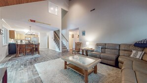 Uma sala de estar ampla com mesa de centro de madeira, sofá de couro e área de jantar com cadeiras de madeira e lustre.