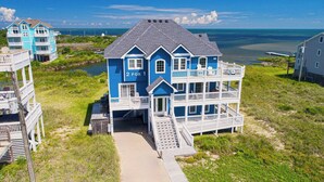 A two-story beachfront house with a balcony, a number '2 for 1' sign, and a view of the ocean. - Premier Oceanfront Dog Friendly w/ Pool, Elevator, Hot Tub, Game and Media Rooms (Hatteras)