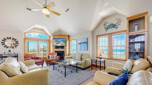 A spacious living room with leather sofas, a glass coffee table, and a fireplace. Large windows offer views of the ocean. - Premier Oceanfront Dog Friendly w/ Pool, Elevator, Hot Tub, Game and Media Rooms (Hatteras)
