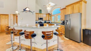A kitchen with a central island, wooden bar stools, stainless steel appliances, and wooden cabinets. - Premier Oceanfront Dog Friendly w/ Pool, Elevator, Hot Tub, Game and Media Rooms (Hatteras)