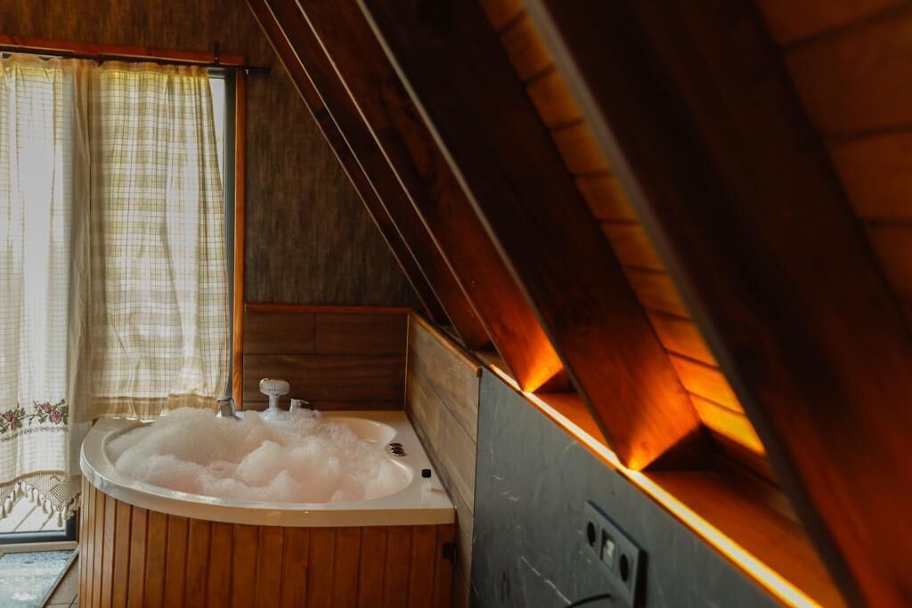 Interior de una cabaña de madera con jacuzzi, paredes de madera y una ventana con cortinas.