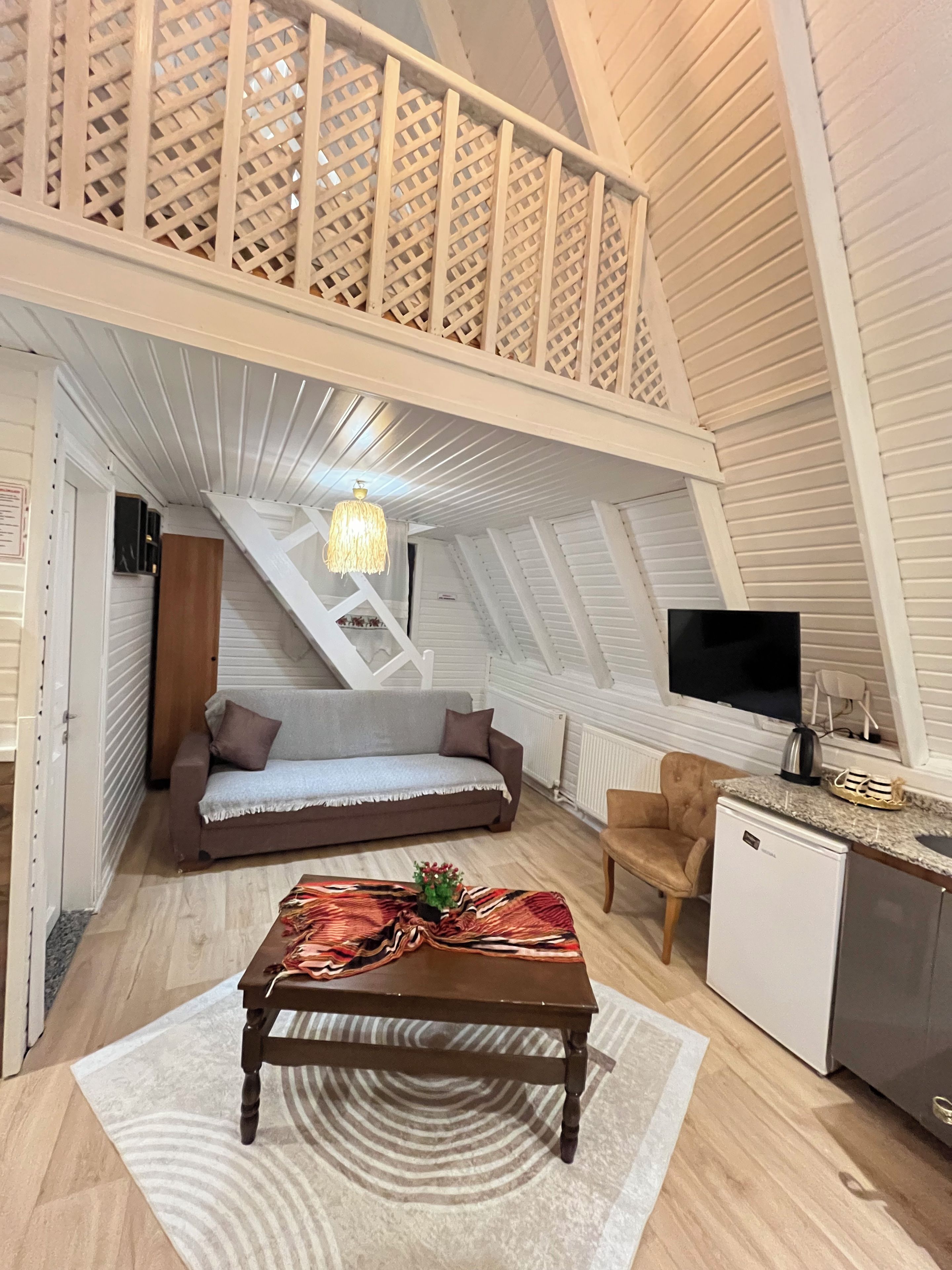 Une pièce de style loft avec un escalier en bois, un canapé, une table basse, un téléviseur et un coin cuisine.