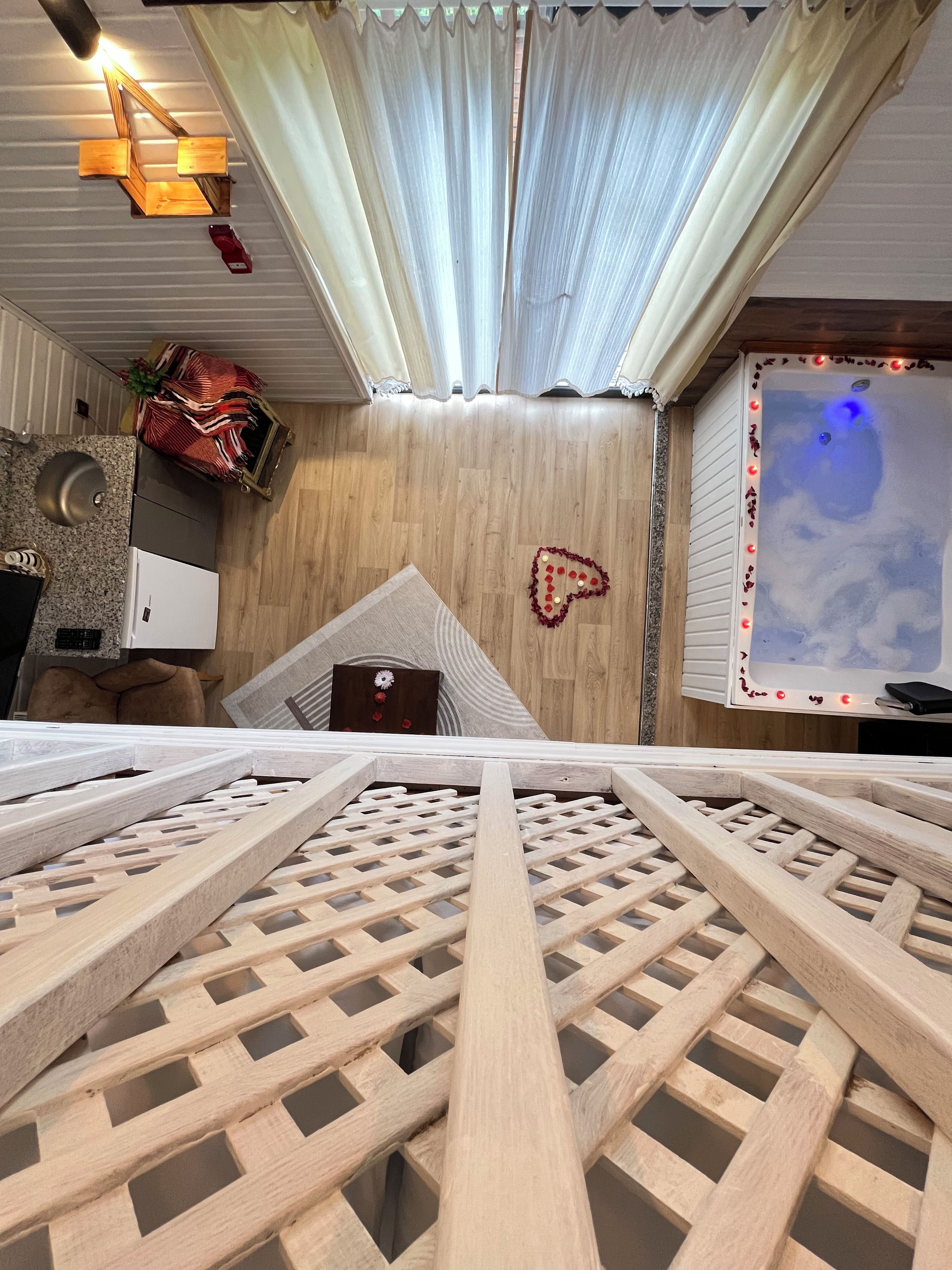 A room with a wooden lattice floor, a ceiling light fixture, a heart-shaped decoration, and a wall-mounted television.