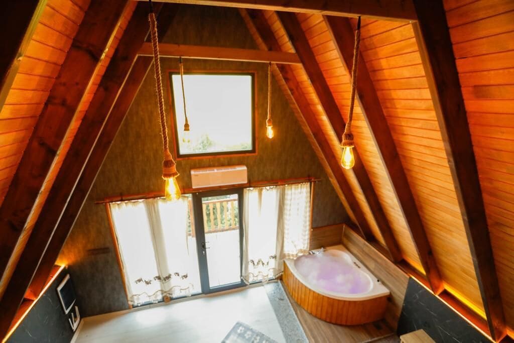 Un dormitorio acogedor en el ático con techo inclinado de madera, un ventanal grande y una bañera empotrada.