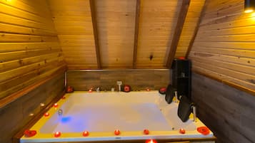 Interior de una cabaña de madera con una bañera grande, velas y un banco de madera.