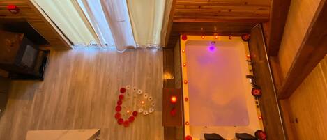A wooden interior with a pool table, a ceiling fan, and a decorative arrangement of red and white flowers.