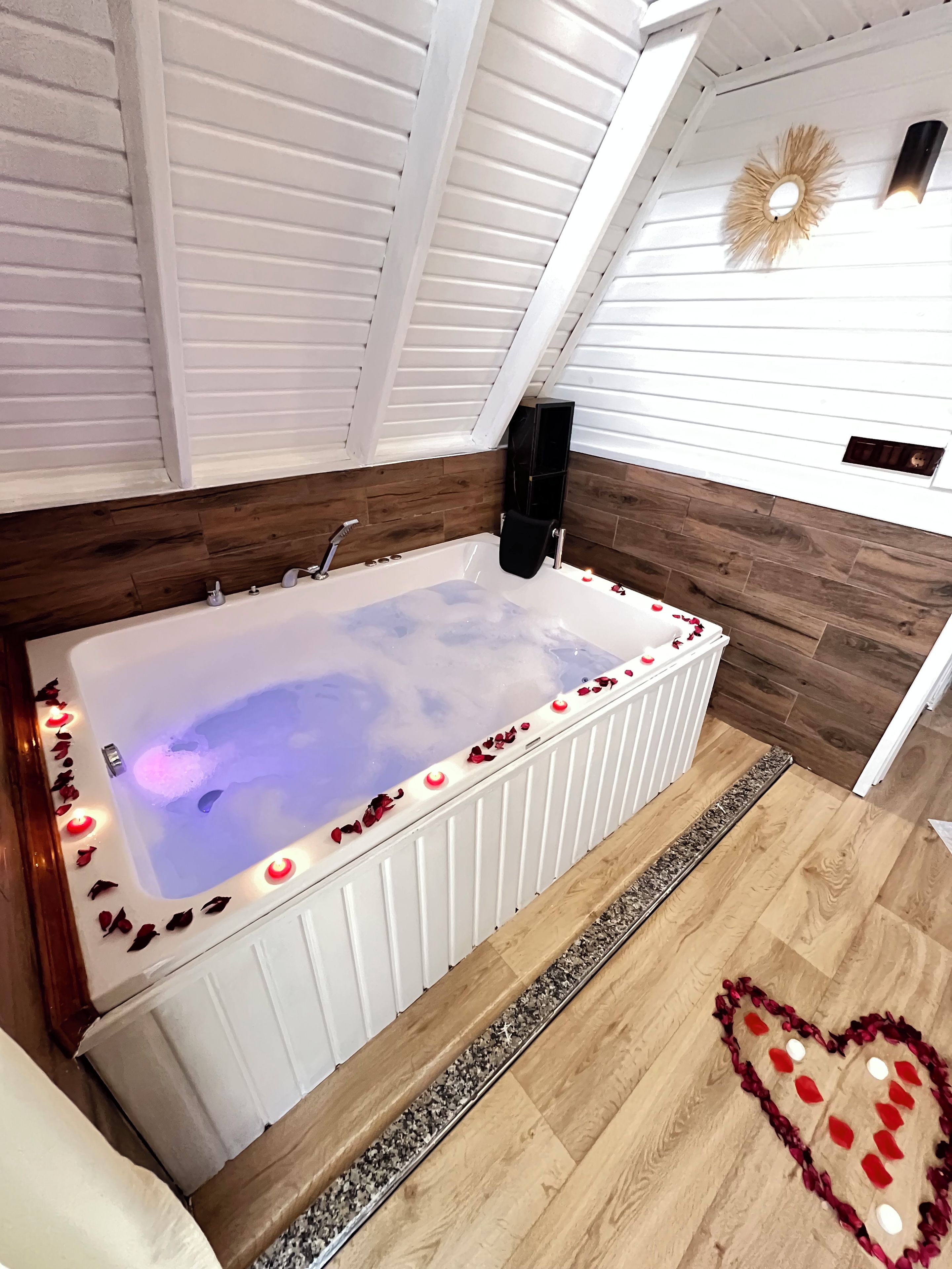 A modern bathroom with a freestanding bathtub, wooden flooring, and a heart-shaped decoration on the floor.