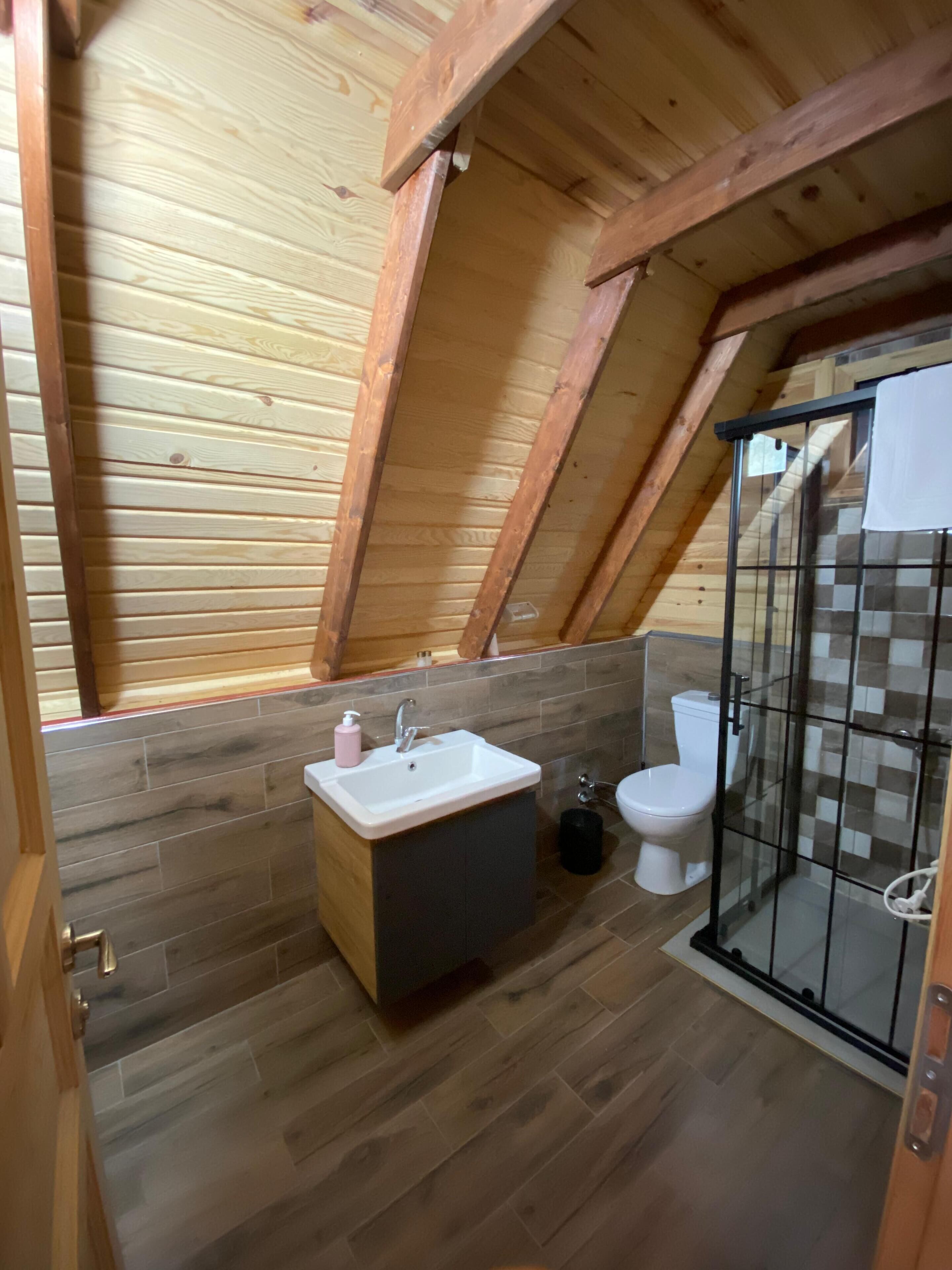 A small, wooden-paneled bathroom with a shower enclosure, a sink, and a toilet.