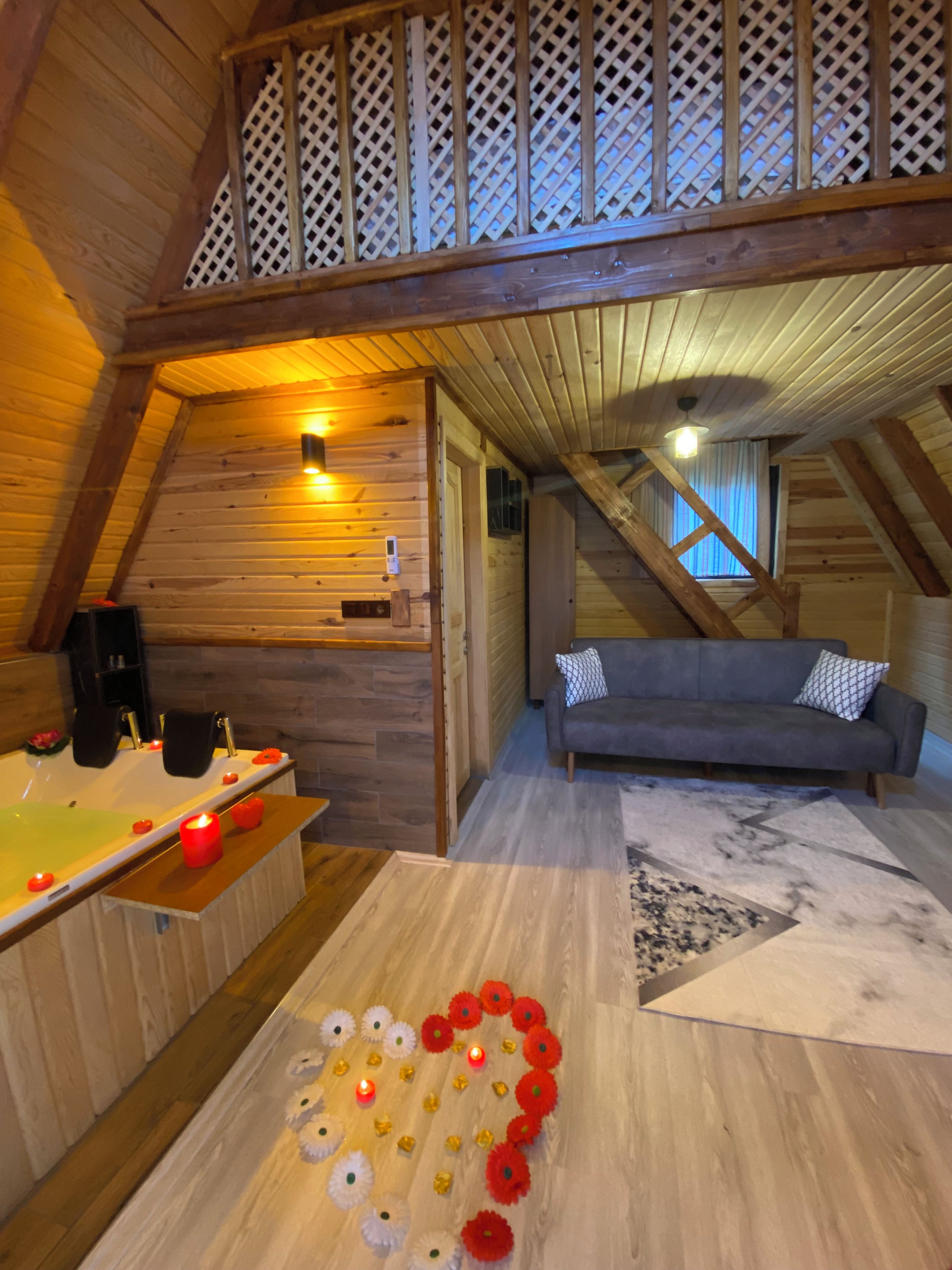 Ein gemütliches Schlafzimmer im Dachgeschoss mit Holzbalkendecke, einer Badewanne, einem Sofa und einer dekorativen Blumenkomposition.
