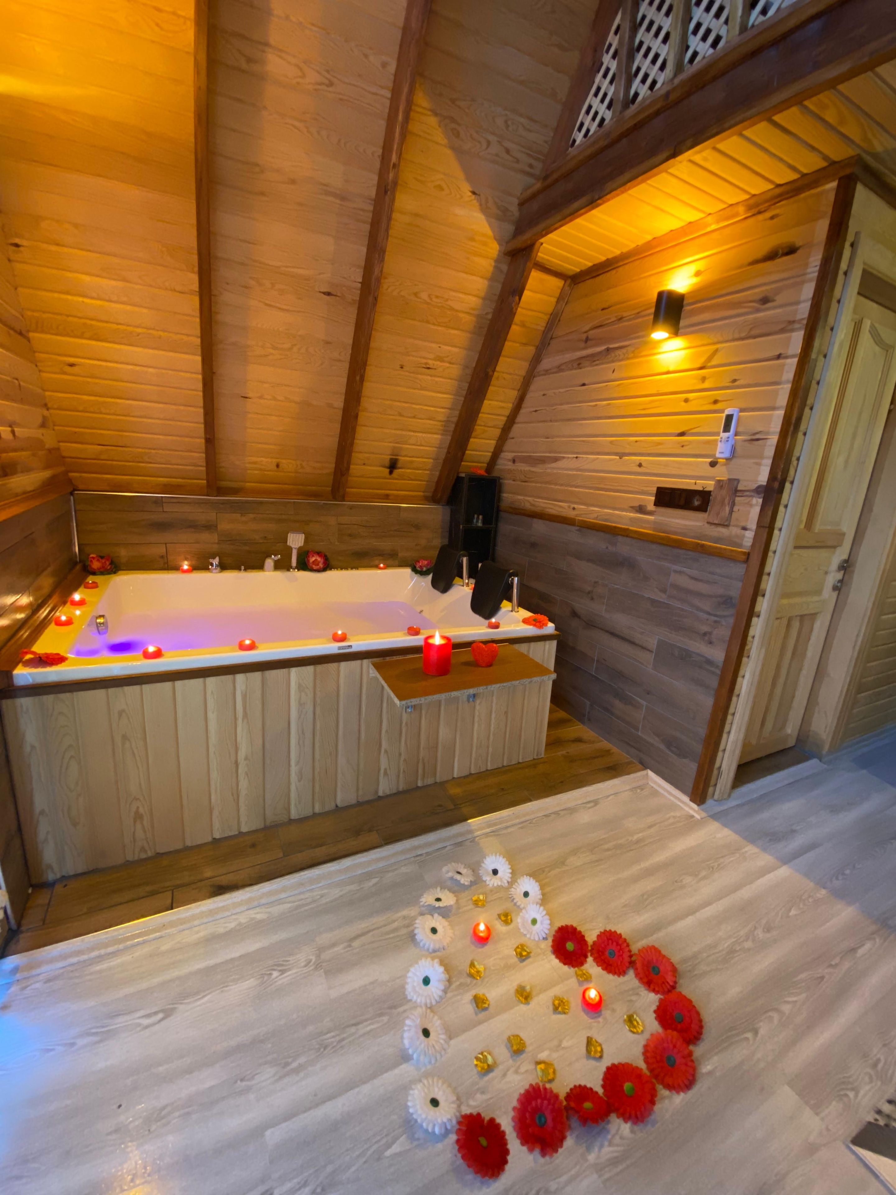 A wooden cabin with a large bathtub, wooden walls, and a ceiling with wooden beams.