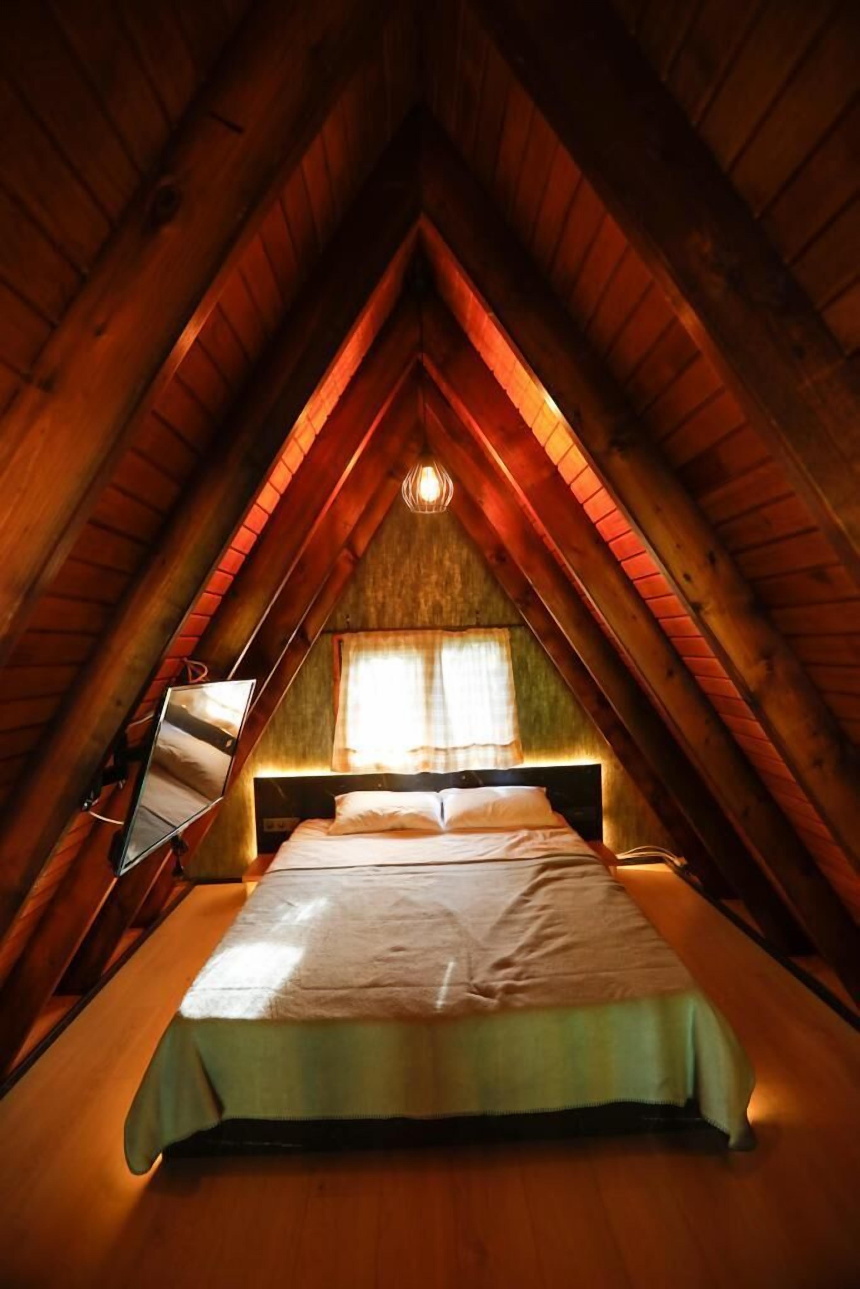 Un dormitorio acogedor en el ático, con techo inclinado, una cama con colcha verde, una mesita de noche y una lámpara colgante.
