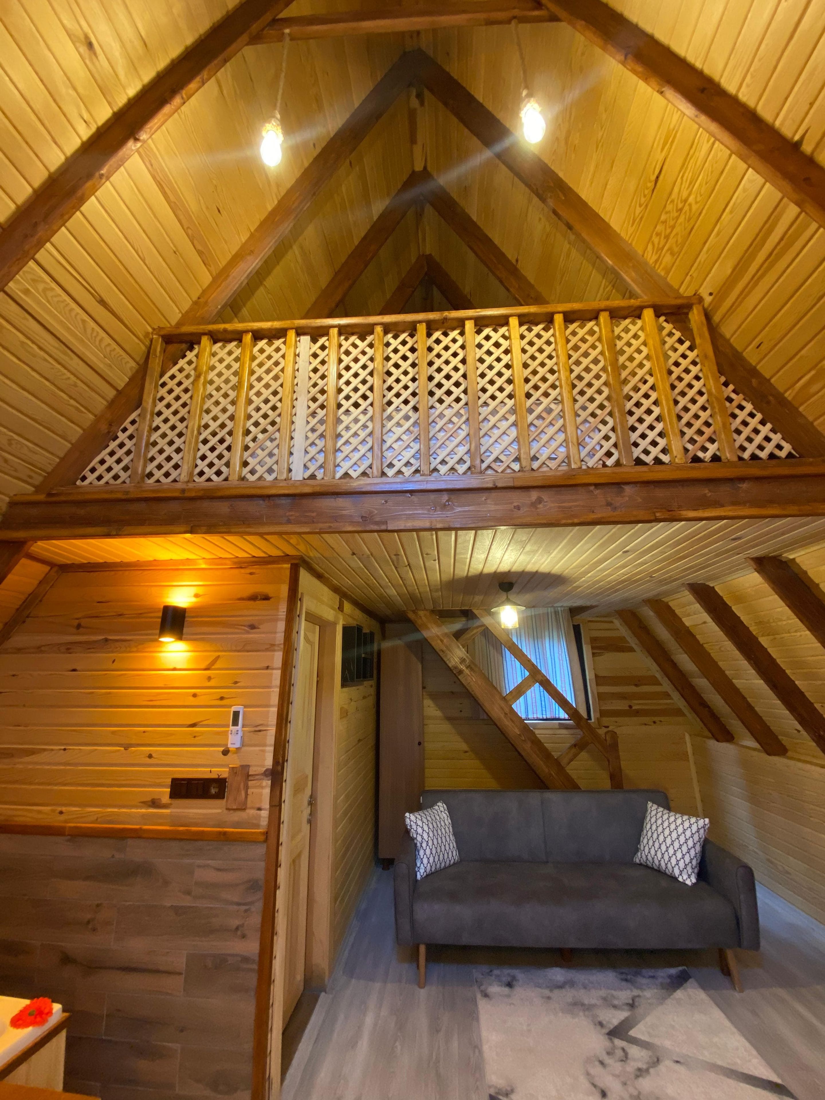 Un interior de madera con un entrepiso para dormir, un sofá y una pequeña mesa.