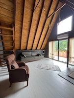 Um amplo quarto no estilo loft, com teto alto, janela grande, sofá, cadeira e escada de madeira.