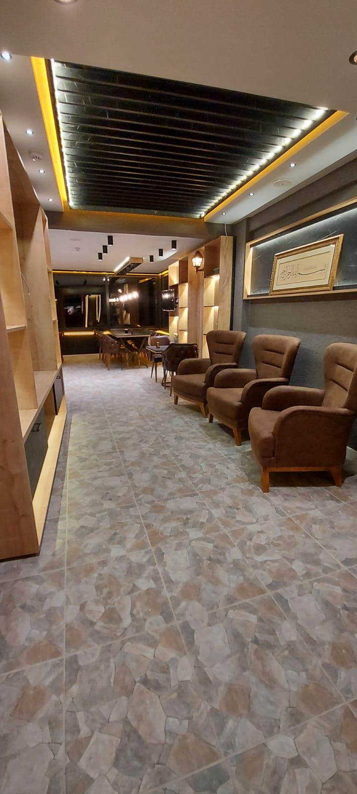 A modern interior with a seating area, stone tile flooring, and a dark ceiling with recessed lighting.