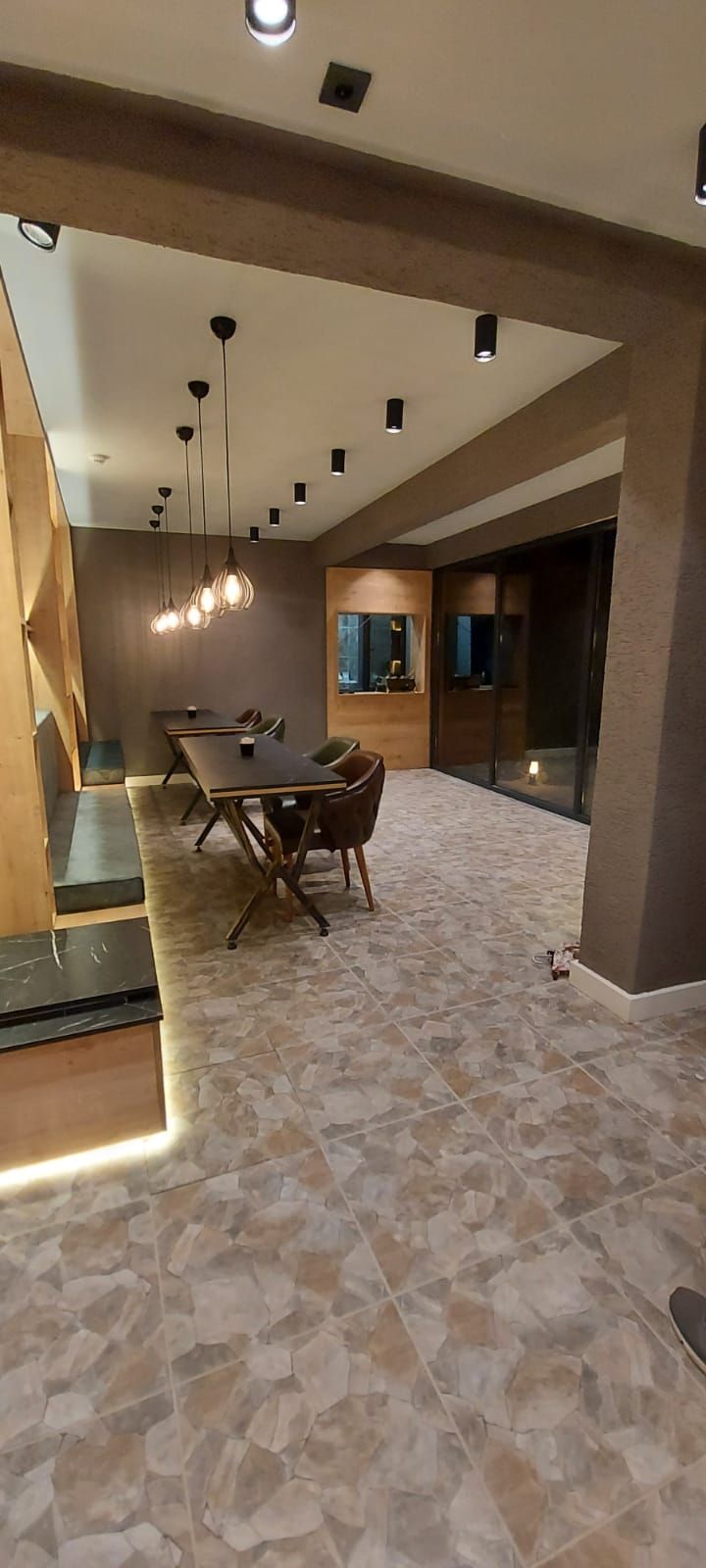 A modern interior with a dining area featuring a long table and chairs, a staircase, and a tiled floor.