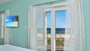 A bedroom with a large bed, a television on the wall, and a view of the beach through the window. - Beachfront, Pet Friendly with 2 Decks~ Windsong (Mexico Beach)