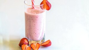 Ett glas jordgubbssmoothie med en jordgubbe som garnering och ett randigt sugrör.