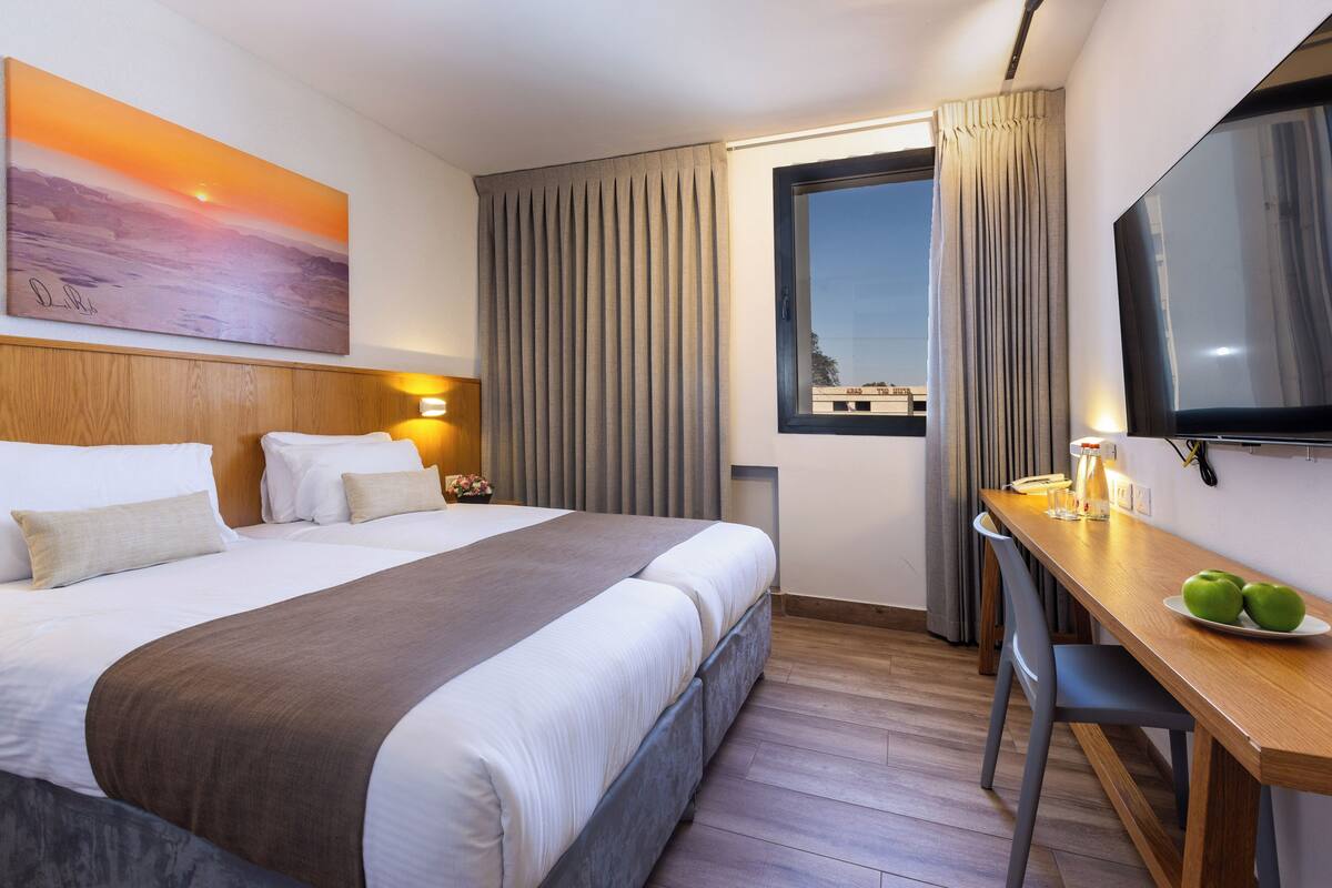 Habitación de hotel con una cama grande, un escritorio con silla, un televisor de pantalla plana y un cuadro en la pared.
