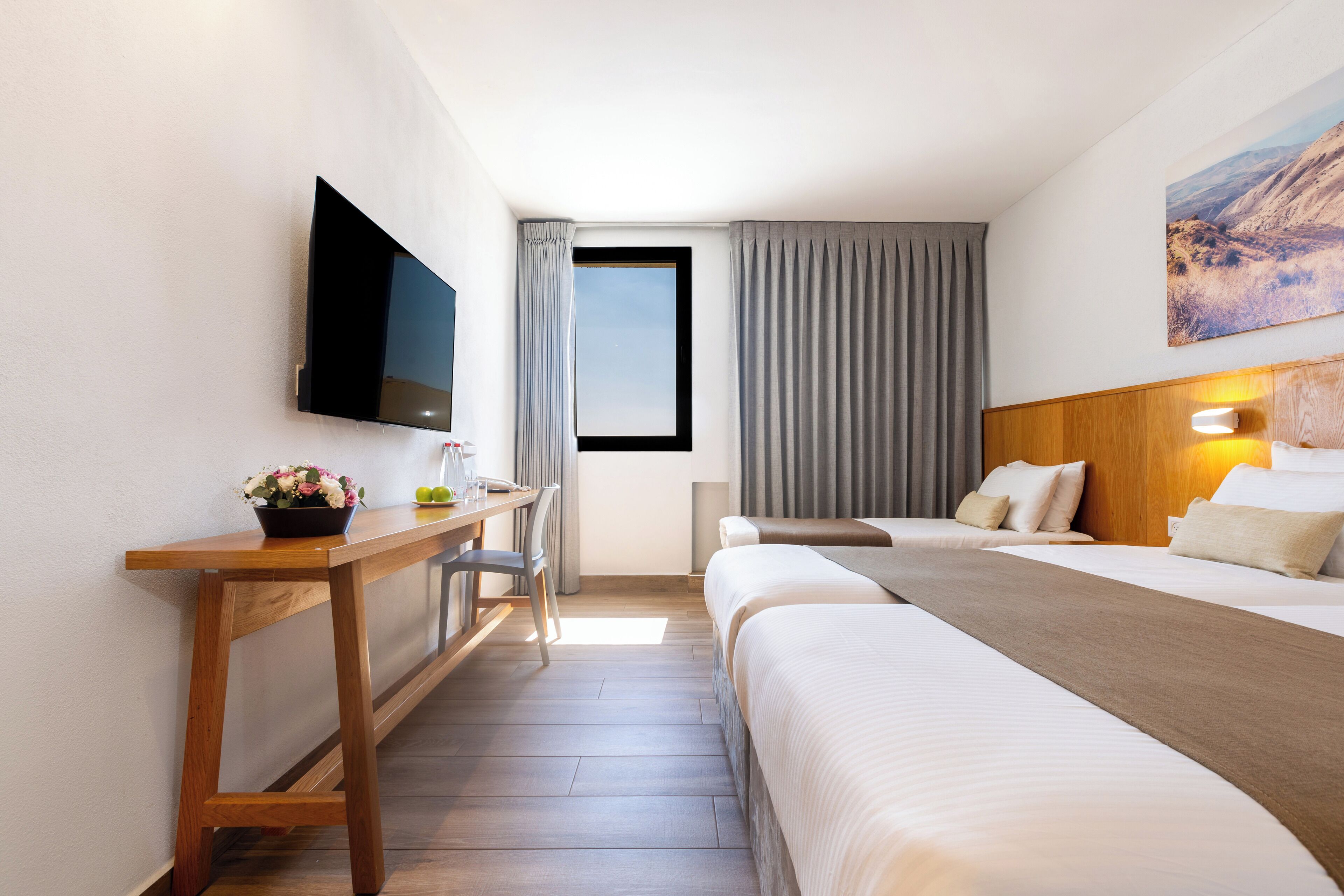 Ein Hotelzimmer mit einem Bett, einem Schreibtisch, einem Sessel, einem Fernseher und einem Fenster mit Vorhängen.