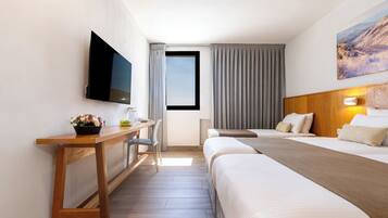 Ein Hotelzimmer mit einem Bett, einem Schreibtisch, einem Sessel, einem Fernseher und einem Fenster mit Vorhängen.