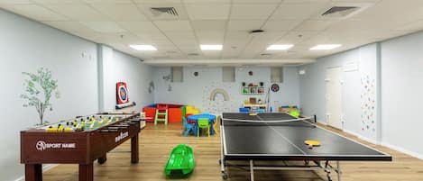 A room with a foosball table, ping pong table, and colorful play area.