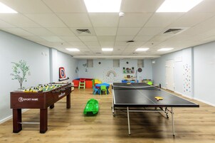 Una habitación con mesa de fútbol de mesa, mesa de ping pong y zona de juegos colorida.