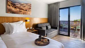 Habitación de hotel con una cama grande, un sofá, una mesa de comedor con sillas, un balcón con vistas y un cuadro en la pared.