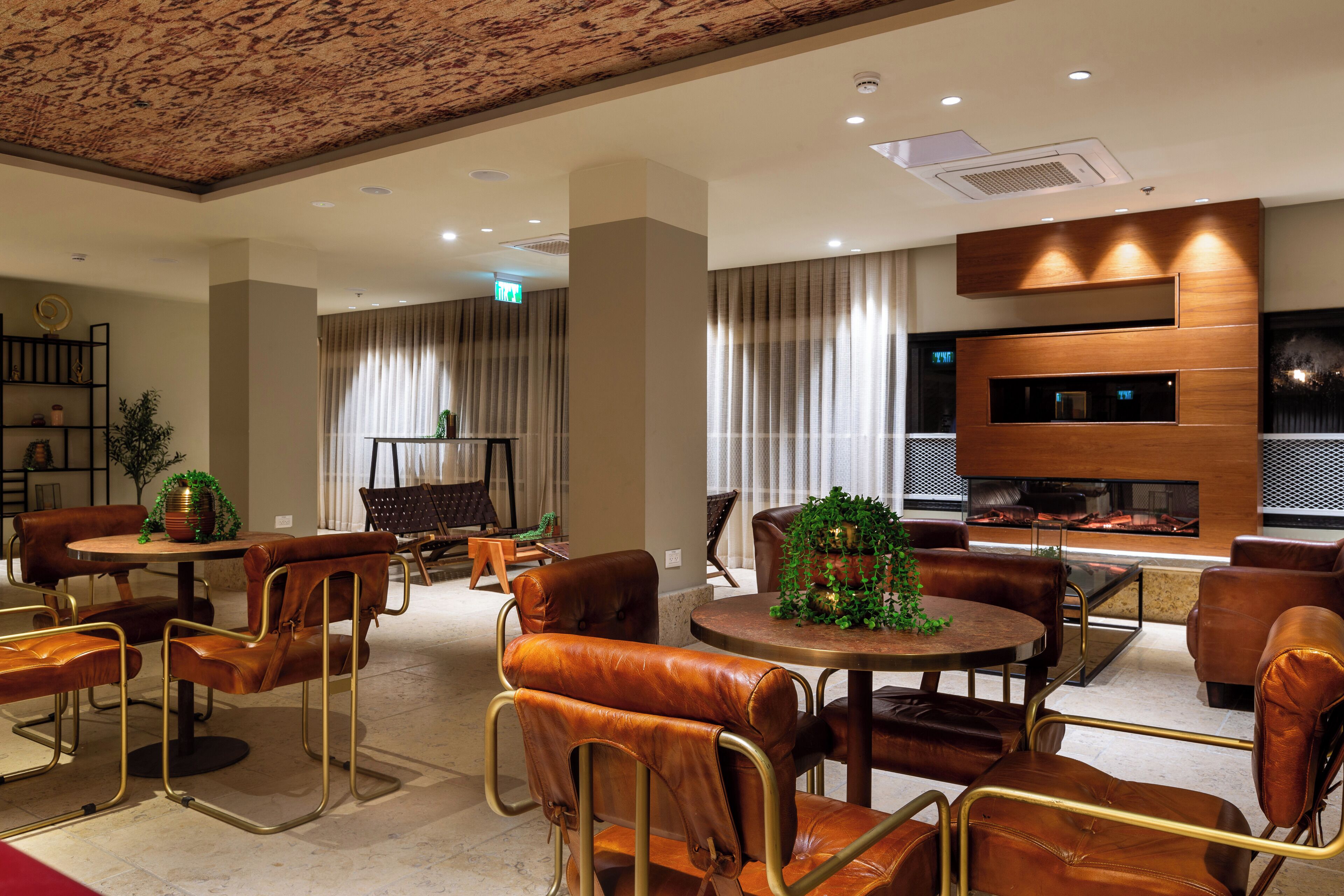 A modern hotel lobby with leather chairs, a round table, a fireplace, and a bookshelf.