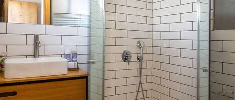 Une salle de bain avec une douche carrelée de carreaux blancs, un meuble-lavabo en bois et une cabine de douche en verre.
