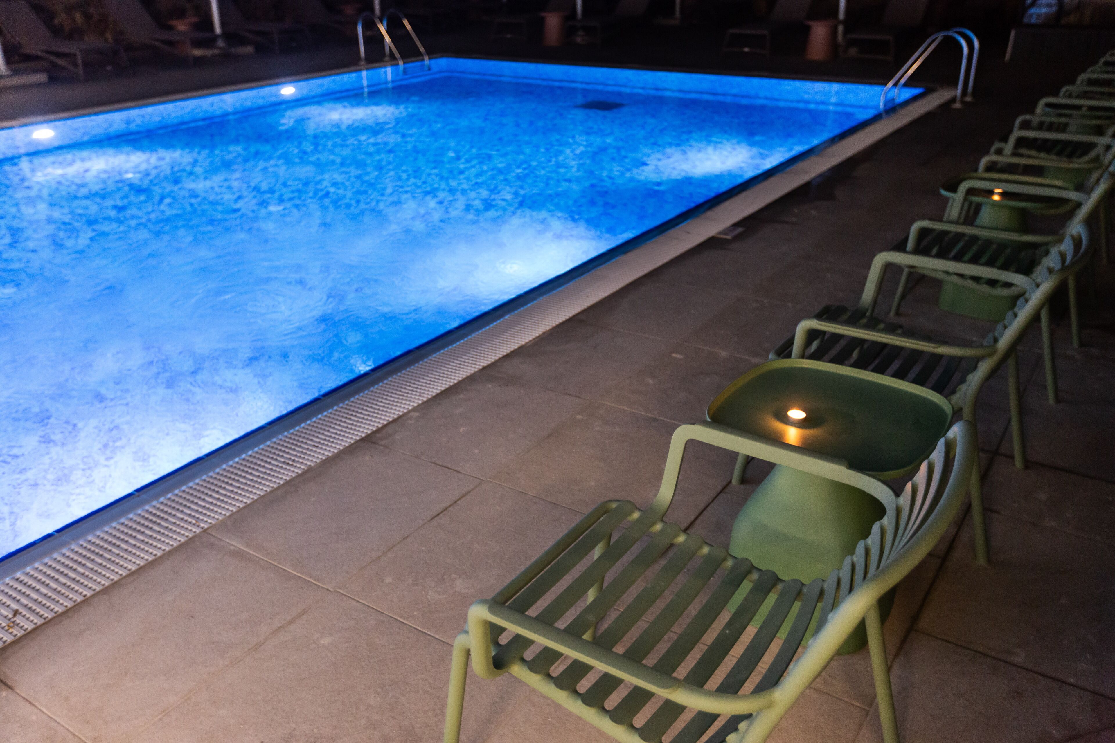 A swimming pool with a tiled deck and green chairs.