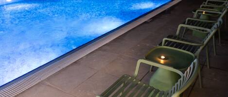 A swimming pool with a tiled deck and green chairs.