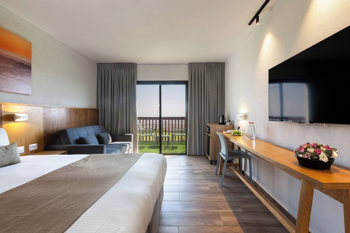Habitación de hotel con cama, escritorio, televisión y balcón con vistas.