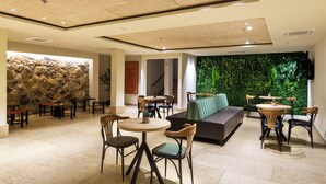 Un área de descanso moderna con paredes de piedra, una pared verde con plantas y una variedad de opciones de asientos, incluyendo mesas y un sofá.