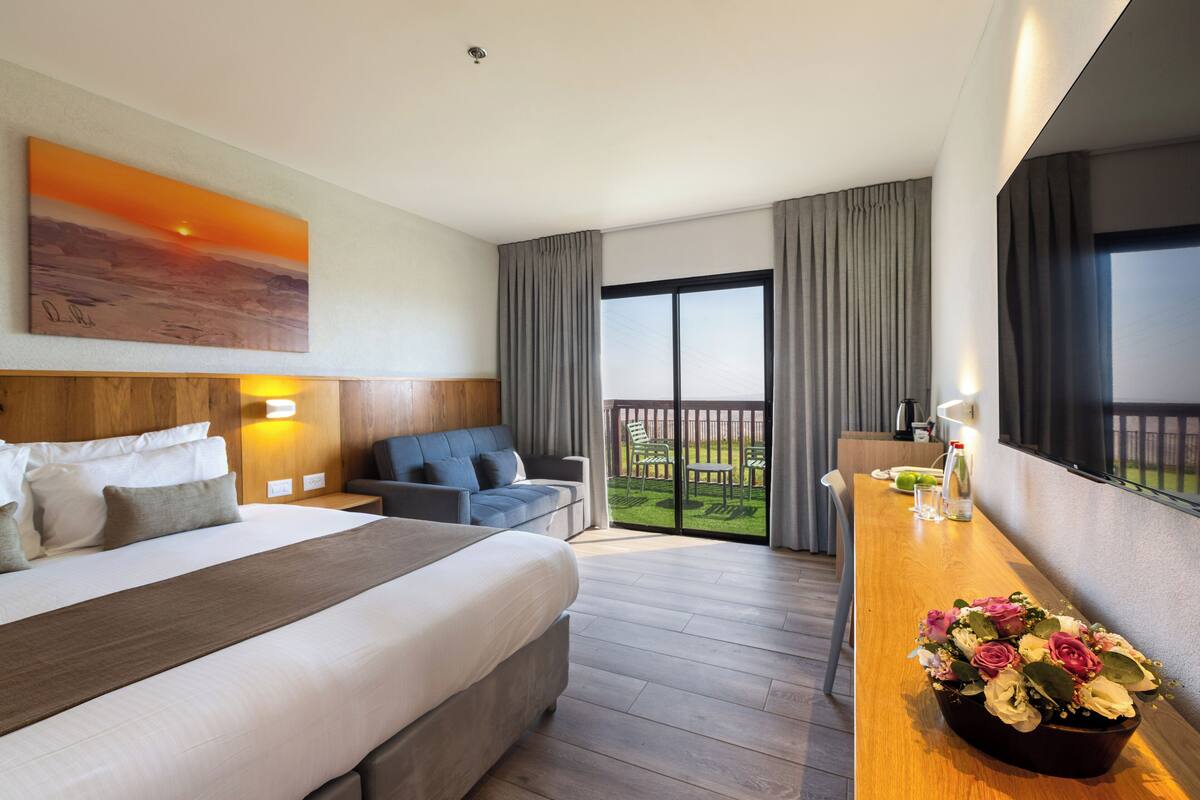 Habitación de hotel con una cama grande, un escritorio con un florero, un cuadro en la pared y un balcón con vistas.
