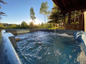 A hot tub with water, surrounded by trees and a stone structure.